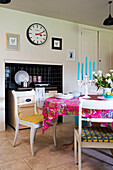 Bunte Stoffe auf Küchentisch und -stühlen mit schwarz gekachelter Ofenmulde in einem Londoner Haus in England UK