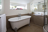 White freestanding roll-top bath in brown panelled bathroom of UK farmhouse