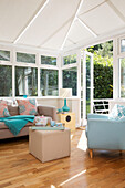 Light blue armchair with sofa in conservatory with open doors to garden, London family home, England, UK