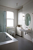 Circular mirror above washbasin in white tiled bathroom of Oxfordshire home England UK