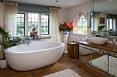 Contemporary freestanding bath with mirrored bathroom cabinet in window of London home, UK