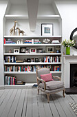 Grey armchair with pink cushion and shelving storage in London townhouse England UK