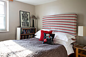 Striped headboard with fur blanket on double bed with bookcase and framed poster in Camber cottage East Sussex England UK