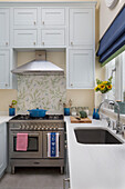 Leaf patterned splashback above range oven in light blue fitted kitchen of London townhouse, England, UK