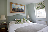 Blattgemusterte Kissen auf einem Doppelbett mit einem Kunstwerk der New Yorker Skyline im Schlafzimmer eines Londoner Stadthauses, England, UK