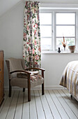 Upholstered chair and floral curtains at window in Presteigne cottage bedroom Wales UK