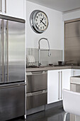 Silver clock above aluminium fitted kitchen with hose tap in contemporary Sussex home, England, UK