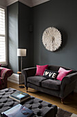 Dark grey two-seater sofa with buttoned ottoman and feather ornament in contemporary Sussex living room, England, UK