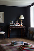 Lamp and books on carved wooden table with figs on ottoman in Sussex living room UK