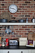 Clock on exposed brick wall with kitchenware on shelves in Shoreham by Sea home   West Susses   England   UK