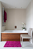 Chair and pink rug at side of wood panelled bath with heated wall radiator in UK home