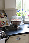 Iced cake on stand with recipe book in Suffolk farmhouse kitchen,  England,  UK