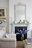 Blue cut flowers in marble fireplace of Hertfordshire living room with cream armchair,  England,  UK