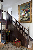 Large framed artwork above wooden staircase in hallway entrance of Sussex cottage   England   UK