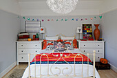 Origami birds above wrought iron bed with pair of bedside chests in London home,  England,  UK