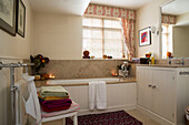 Folded towels on pew chair in bathroom with lit candles,  London home,  England,  UK