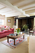 Red sofa and wooden coffee table with exposed brick fireplace in living room of UK farmhouse