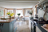Open plan beamed kitchen with pan rack above range oven in UK farmhouse