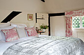 Toile de jouy curtain and cushion fabric in timber-framed bedroom of UK farmhouse
