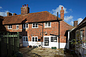 Paved backyard and sunlit exterior of brick London home with tiled roof and chimneys,  UK