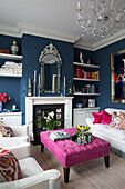 Crystal chandelier above pink ottoman in blue living room of London home,  England,  UK