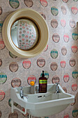 Convex mirror above washbasin with patterned wine label wallpaper in Surrey home,  England,  UK