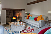 Labrador lies in front of lit woodburner in Surrey living room with colourful cushions England,  UK