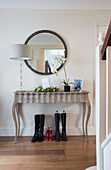 Orchid and lamp on console with circular mirror and wellington boots in hallway of London home   England   UK