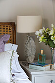 Feather lampbase and perfume bottle with cut flowers on bedside cabinet in London home   England   UK