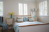 Floral cushions on bed with matching cabinets with shuttered windows in London home   England   UK