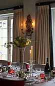 Beleuchtete Kerzen mit weißen Rosen in silberner Vase auf dem Esstisch zu Weihnachten in einem Haus in Lymington, Hampshire, Großbritannien