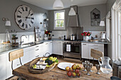 Large vintage clock above sink in Berkshire kitchen with stainless steel extractor,   England,  UK