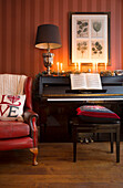 Red leather armchair beside piano with lit candles in Surrey home   England   UK