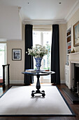 Vase mit Gänseblümchen auf hölzernem Sockeltisch im Wohnzimmer mit blauen Vorhängen in einem Londoner Stadthaus England UK