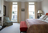 Cream curtains at French windows with buttoned seat at foot of double bed in London townhouse   England   UK