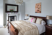 Gold metallic lampshades with polished wooden sleigh-bed and Victorian fireplace in contemporary London home, England, UK