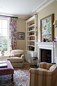 Bookcase and artwork with armchairs at fireside in Pewsey country house Wiltshire England UK