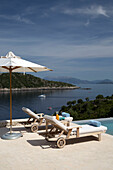 Sunloungers and parasol at poolside with view of Aegean sea on Greek island of Ithaca