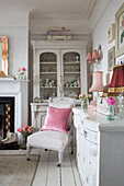 Pink cushion on upholstered chair with glass fronted cabinet in Norfolk home England UK