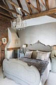 Glass chandelier hangs above grey double bed in beamed Wokingham cottage bedroom Berkshire UK