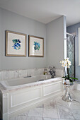 Framed artwork with orchid on metal side table in marble bathroom of London townhouse England UK
