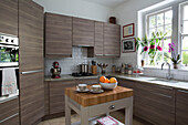Cut flowers on windowsill in wood fitted kitchen of London townhouse England UK