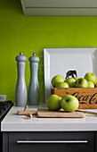 Salt and pepper grinders with apples on chopping board in lime green Surrey kitchen England UK