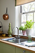 Copper pan next to sink with herbs at windowsill in Dorset kitchen England UK