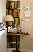 Weidenlampe und Karaffe auf Beistelltisch mit Bücherregal in einem Haus in Dorset, England, UK