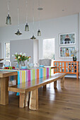 Pendant lights hang over wooden table with bench seats and striped cloth in Lechlade home Gloucestershire England UK
