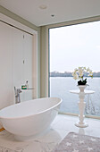 Freestanding bath with orchid on table at full length window in Lechlade home Gloucestershire England UK