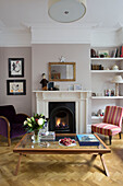 Sessel und Couchtisch mit beleuchtetem Kamin im Wohnzimmer eines viktorianischen Familienhauses in South West London UK