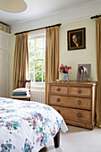 Wooden chest of drawers with curtains at window in Georgian Berkshire home England UK