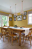 Pendant shades hang above wooden table in yellow dining room of Georgian home Berkshire England UK